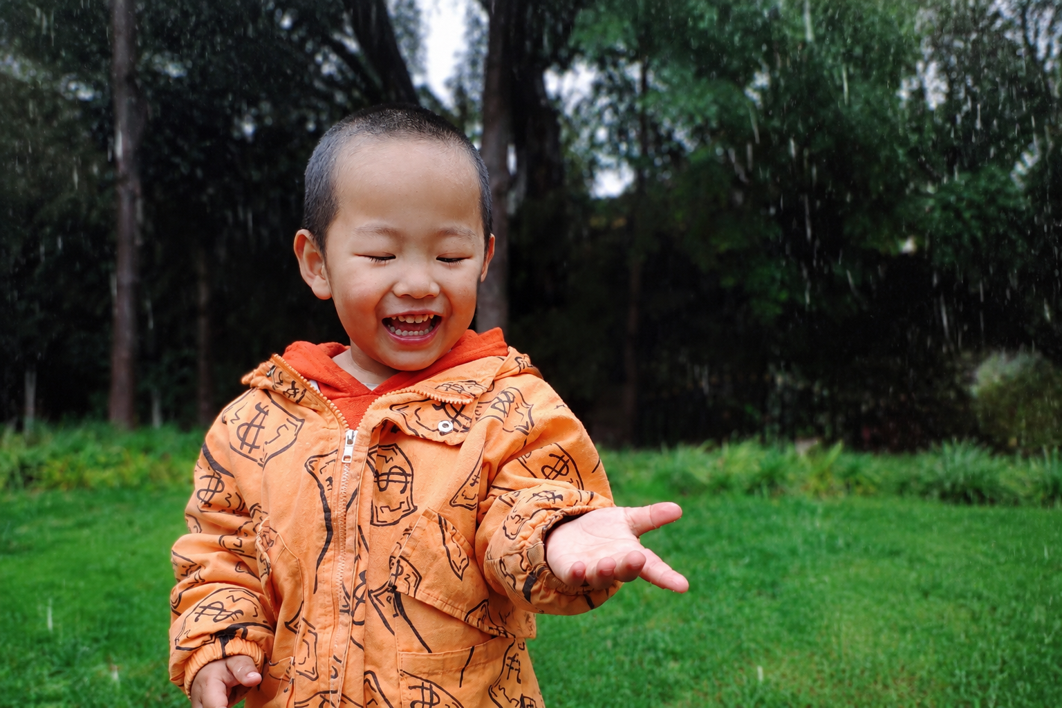 生活抓拍風(fēng)格，一個(gè)活潑的2歲多小男孩在戶外下雨天開心地伸出手接雨滴，笑容天真燦爛，展現(xiàn)出寶寶在強(qiáng)大免疫力保護(hù)下，無懼風(fēng)雨、親近大自然的戲精與活力日常。