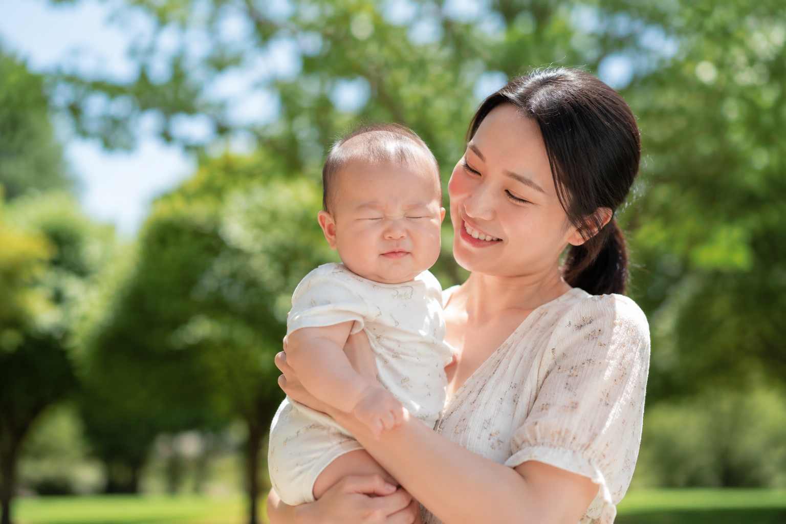 A photorealistic, high-quality image of a beautiful Chinese mother holding her cute 6-month-old baby in a sunny park during early summer. The sun is shining brightly overhead. The baby is squinting their eyes slightly due to the strong sunlight, looking cute but mildly uncomfortable. Lush green trees in the blurred background. Cinematic lighting, soft shadows, shot on 85mm lens, highly detailed, 8k resolution. --ar 3:4