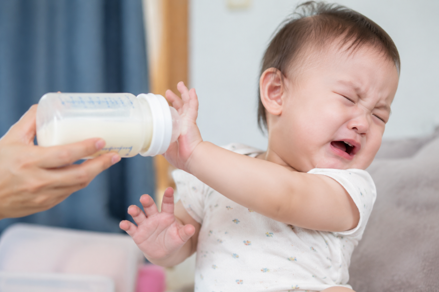 A hyper-realistic close-up photography of a cute 1-year-old Chinese baby crying and drooling, turning head away and refusing a baby bottle gently offered by a mother's hand. Natural indoor lighting, bright and soft tones, high resolution, 8k, photorealistic, emotional --ar 3:4