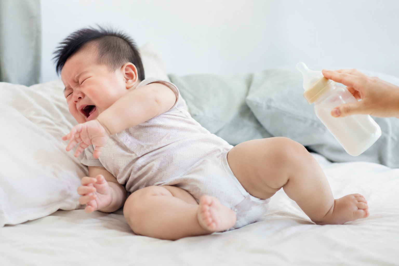 A cute Chinese baby, around 5 months old, wearing a light summer onesie, lying on a soft bed, turning head away from a baby bottle, crying and arching back, looking fussy, bright natural lighting, soft colors, highly detailed, 8k resolution, photorealistic, photography --ar 3:4
