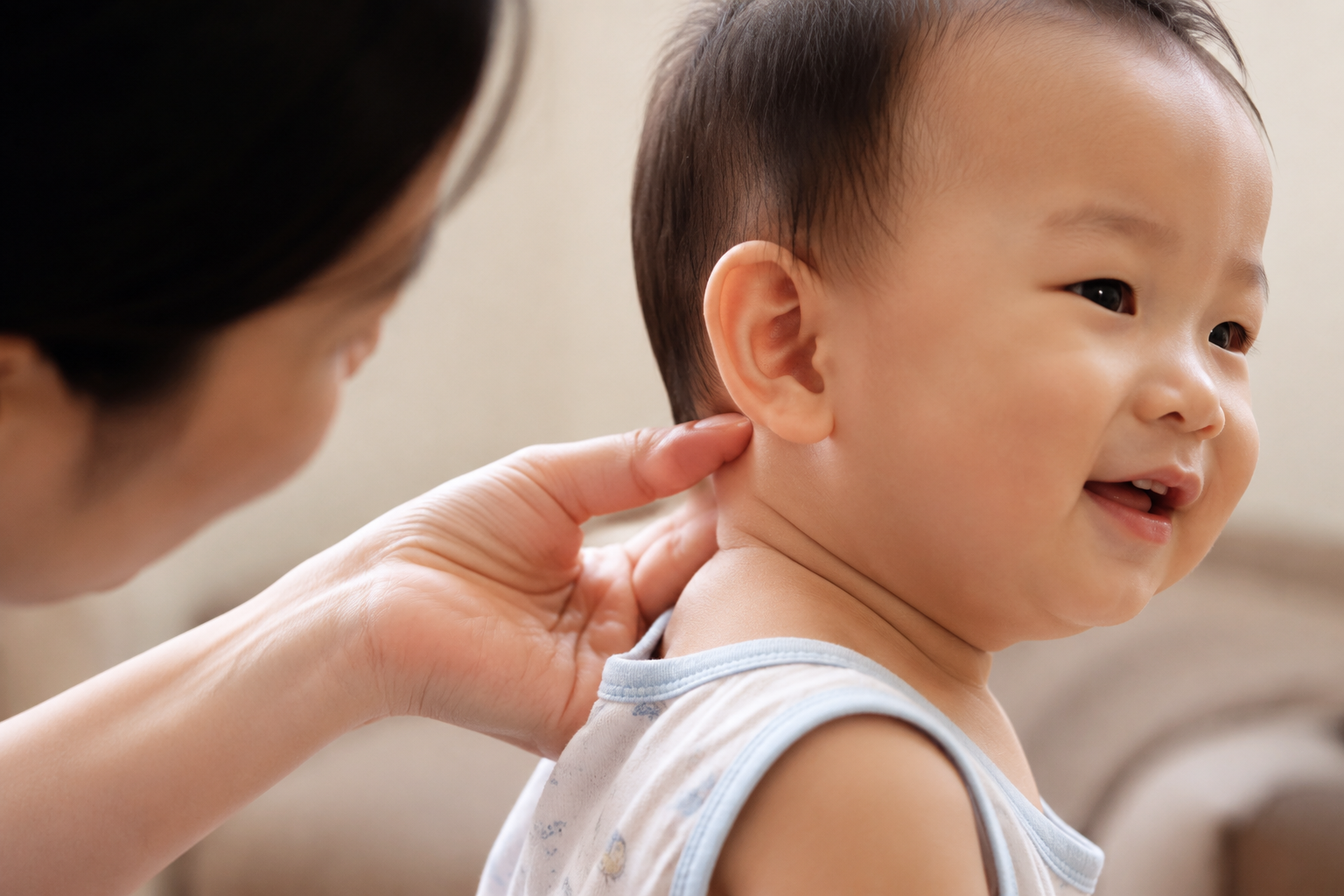 A close-up shot of a gentle Chinese mother's hand reaching into the back of the neck of a smiling 1-year-old Chinese baby to check the temperature. The baby is wearing a light summer outfit. Warm and loving atmosphere, soft natural indoor lighting, shallow depth of field focusing on the hand and the baby's neck, highly detailed skin texture, photorealistic, 8k.