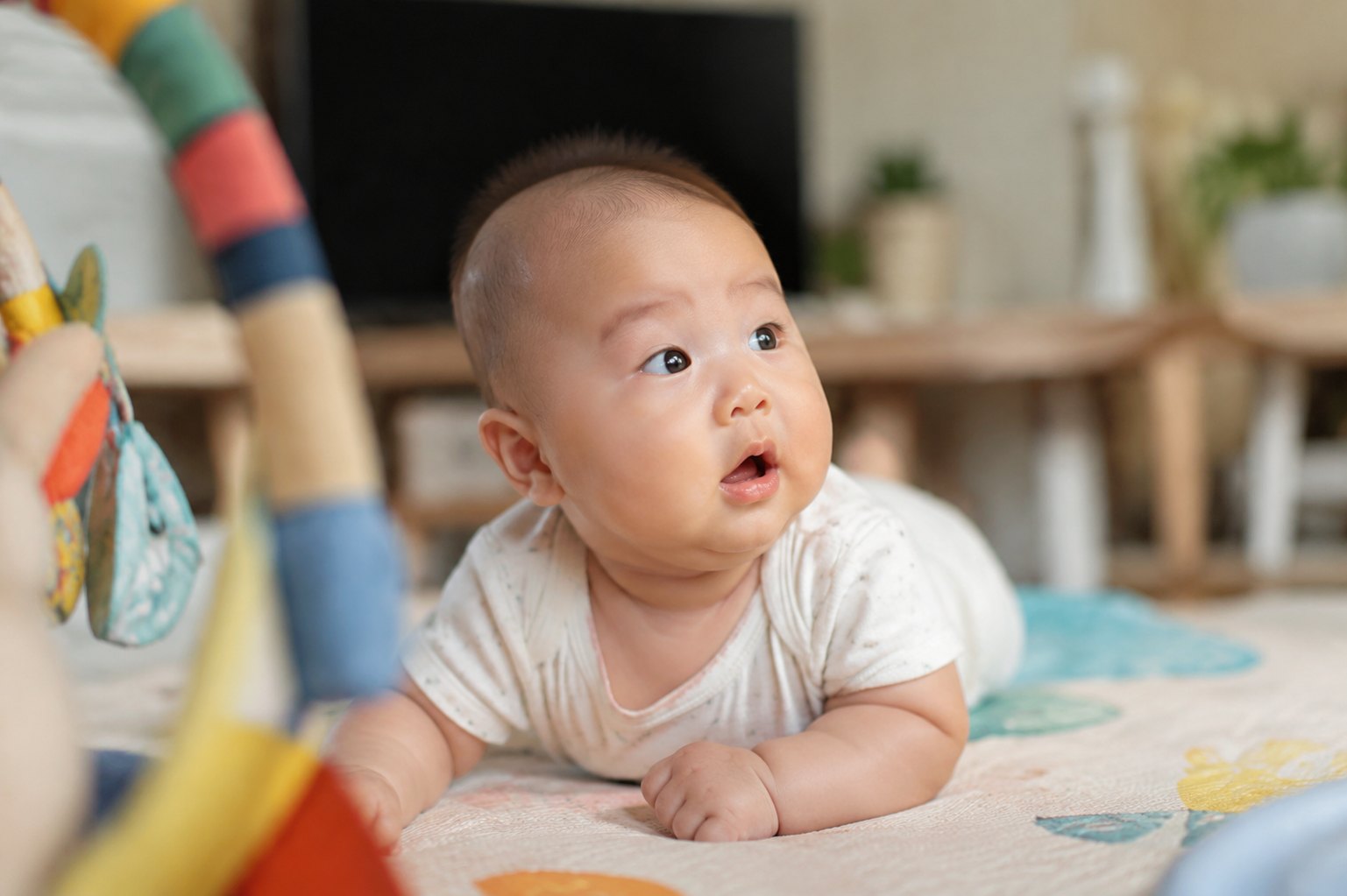 A cute 5-month-old Chinese baby lying on a soft cozy play mat, turning head curiously to look at a sound source off-camera. Wide bright eyes, alert, adorable and engaged expression. Warm natural lighting, soft focus background of a cozy living room, photorealistic, captured with a DSLR camera, 85mm lens, f/1.8 --ar 3:4