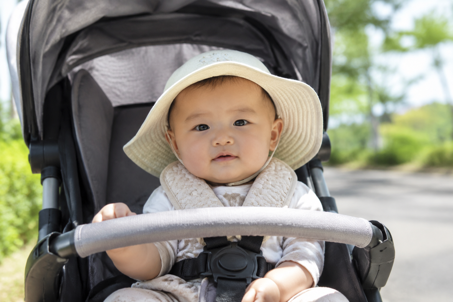 A cute 4-month-old Chinese baby sitting in a baby stroller, wearing a wide-brimmed sun hat, the stroller has a sunshade canopy, sunny summer day, soft natural lighting, high quality, photorealistic, 8k resolution --ar 3:4