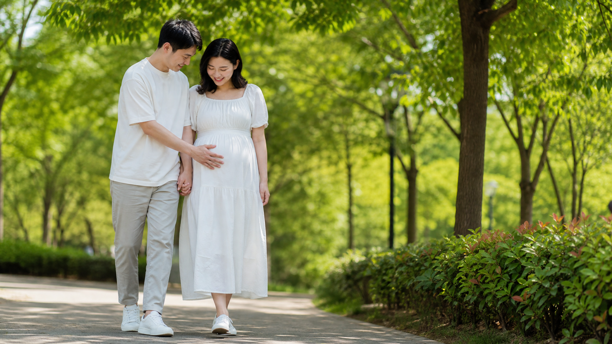 A happy Chinese pregnant couple walking hand in hand in a sunny green park, the husband gently touching his wife's baby bump, wearing comfortable casual summer clothes, lush green trees, bright daylight, optimistic and healthy vibe, photorealistic, 8k, highly detailed.