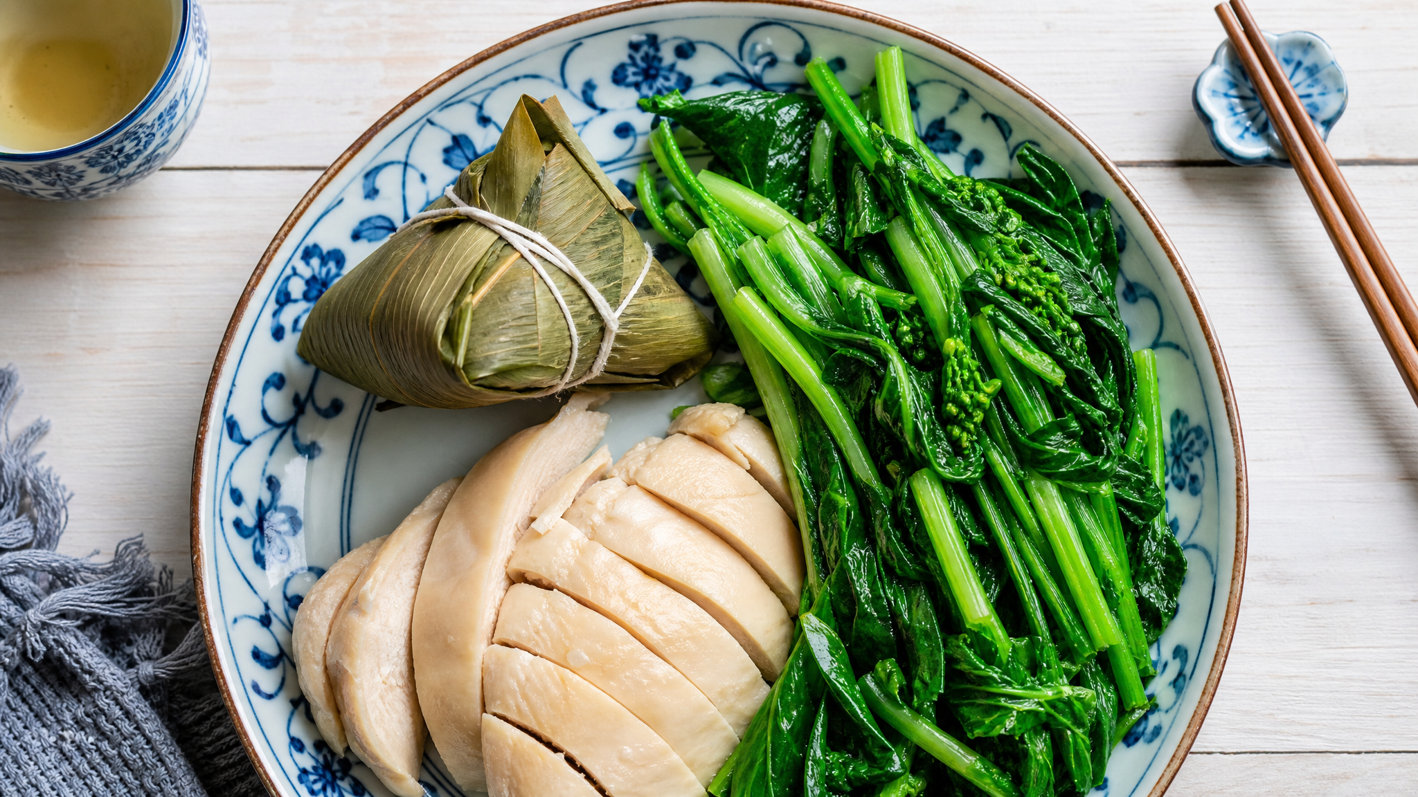 A flat lay top-down view of a healthy pregnancy meal. A small unpeeled Zongzi (sticky rice dumpling) next to a portion of boiled chicken breast and a large portion of fresh green leafy vegetables on a beautiful ceramic plate. Chinese dining style, bright and clean food photography, natural lighting, highly detailed, appetizing, 8k.