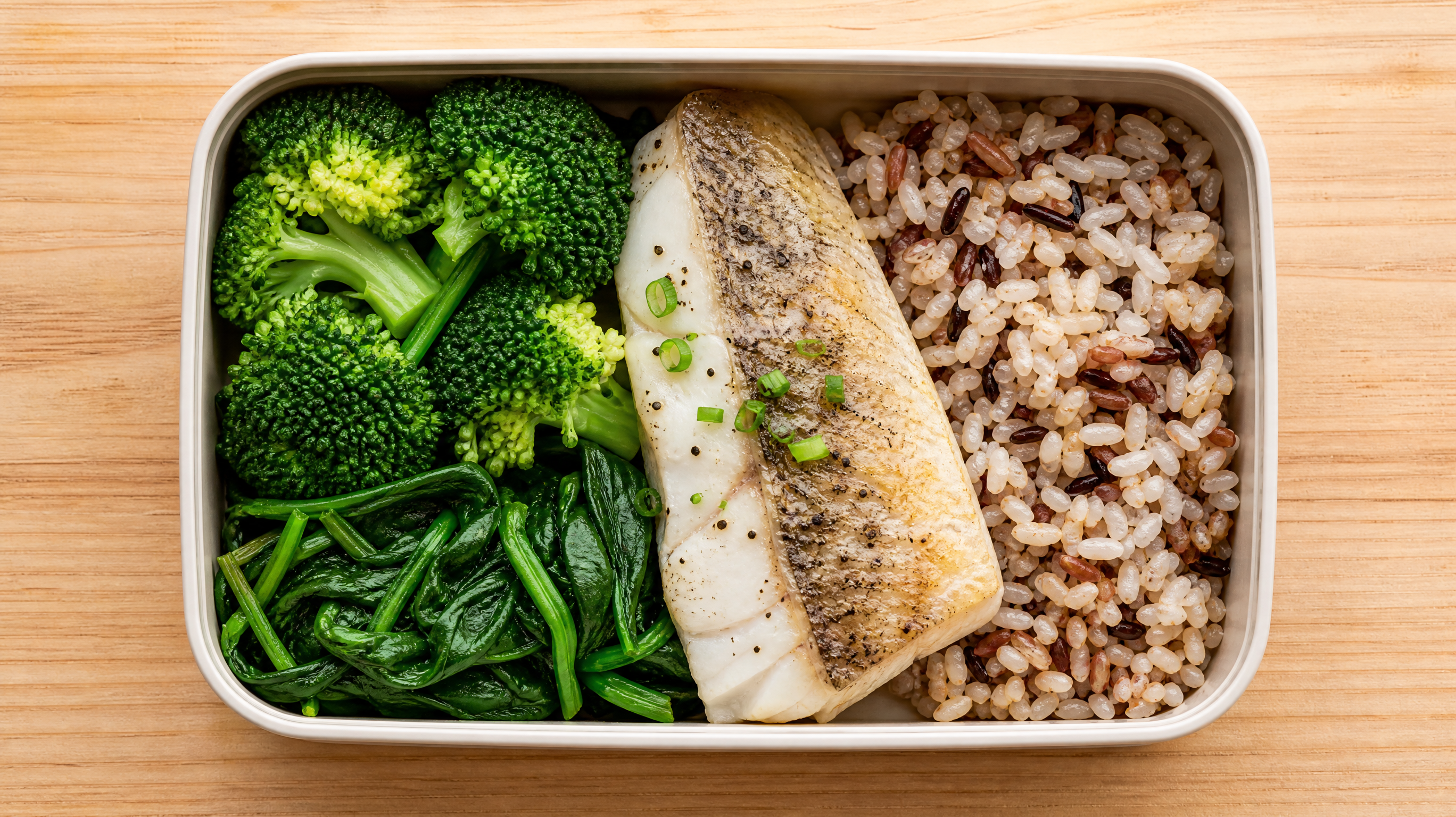 A top-down view of a beautifully arranged healthy lunch bento box on a light wooden table. The box contains a palm-sized portion of steamed sea bass, two fistfuls of fresh green vegetables like broccoli and spinach, and a small portion of mixed whole grain rice. Bright, fresh colors, appetizing food photography, soft studio lighting, high quality, hyper-realistic.
