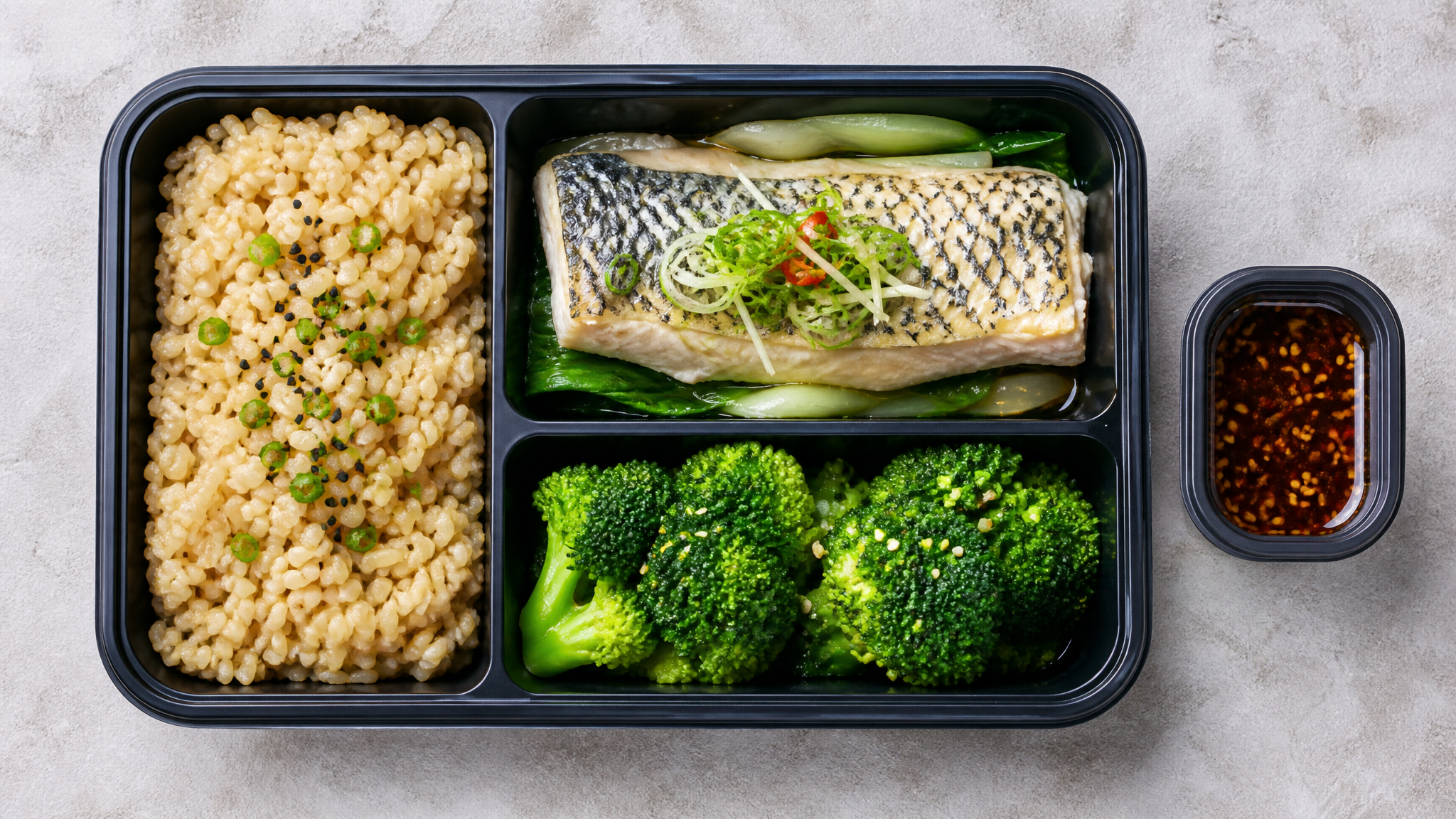 Top-down view of a delicious and healthy Japanese-style bento box, featuring steamed sea bass, brown rice, and fresh broccoli. The bento has clear partitions. Next to it is a small separate sauce container. Bright studio lighting, food photography, appetizing, highly detailed, 8k, realistic textures.