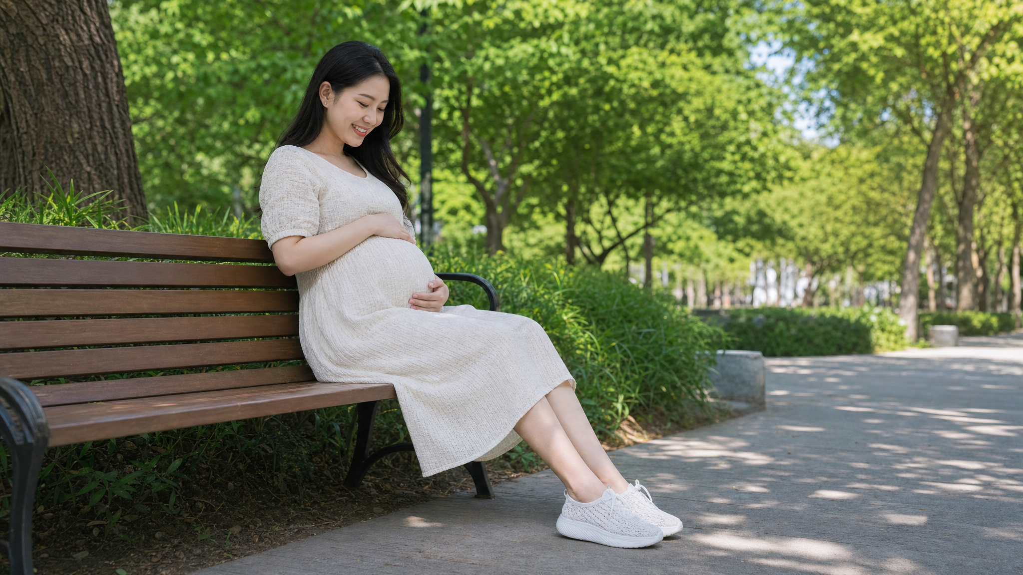 A beautiful Chinese pregnant woman sitting on a park bench in early summer, wearing a comfortable light-colored summer dress and breathable white knitted sneakers. She is gently touching her belly with a relaxed and happy smile. Soft sunlight filtering through the leaves, bright and fresh atmosphere, photorealistic, 8k resolution, highly detailed, shot on 35mm lens.