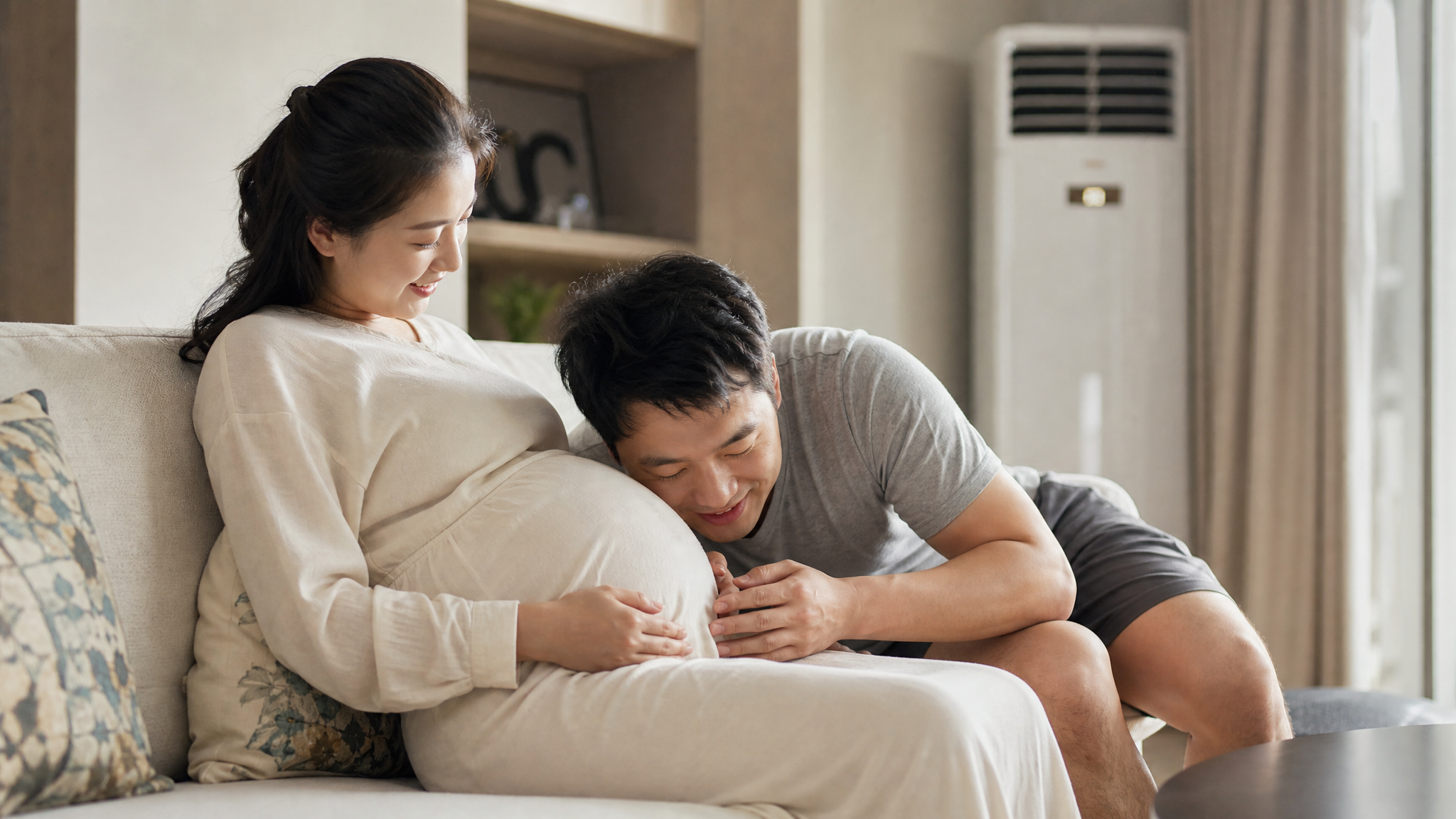 A warm and cozy photography of a beautiful Chinese pregnant woman resting comfortably on a sofa in a modern aesthetic living room, a gentle air conditioner is visible in the background. A loving Chinese husband is leaning close to her belly, smiling and talking softly to the baby. Soft natural indoor lighting, high quality, cinematic, realistic, heartwarming family moment, 8k. --ar 3:4