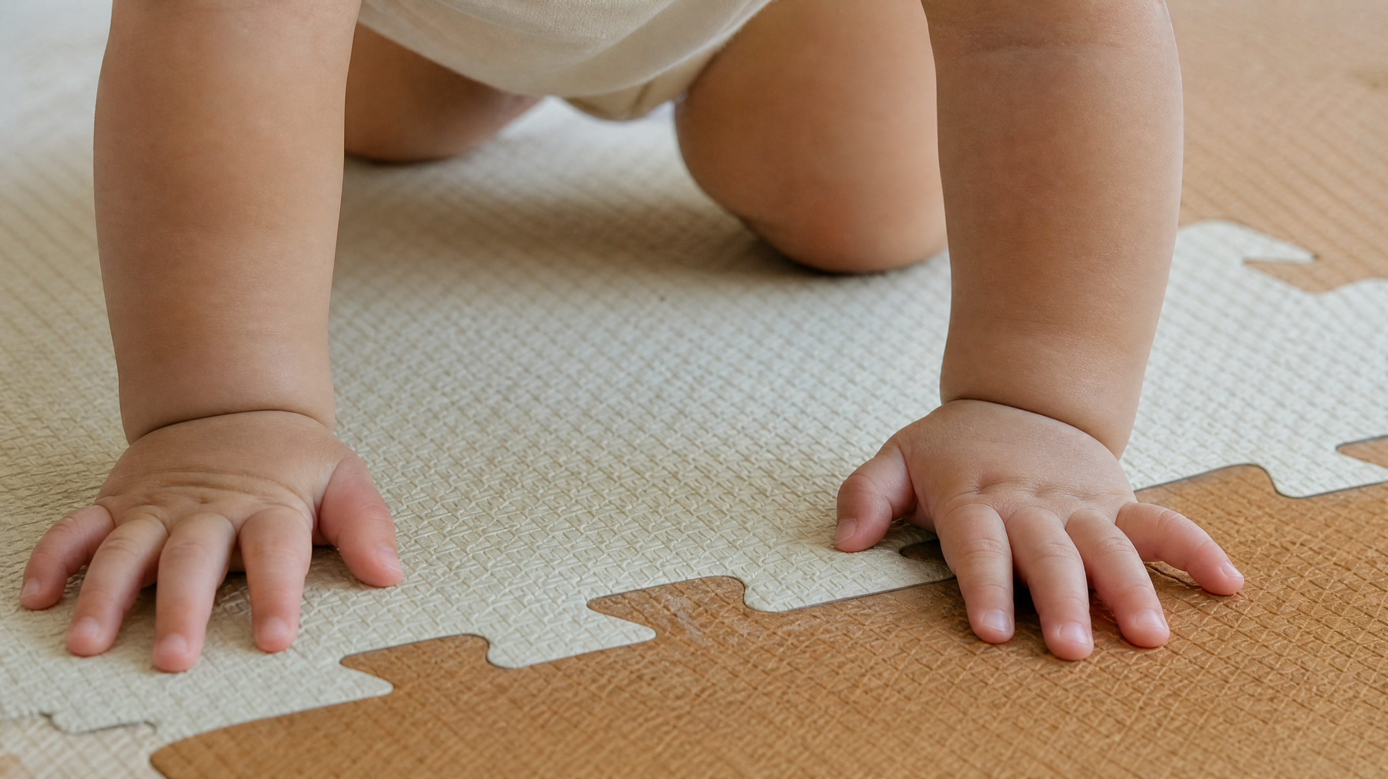 Close up of a Chinese baby's chubby hands and knees crawling on a firm textured EVA puzzle play mat. Soft indoor lighting, focus on the grip and texture, warm tones, high quality, 8k, photorealistic.