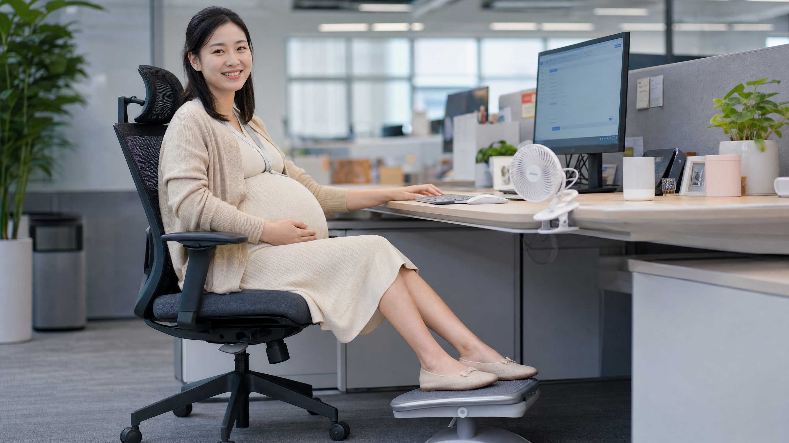 A smiling Chinese pregnant woman sitting at a modern office desk, wearing comfortable maternity clothes. Her feet are resting on a small ergonomic footstool. A small clip-on fan is attached to the desk blowing gently. Bright office lighting, clean and professional environment, realistic photography, high quality, 8k. --ar 3:4