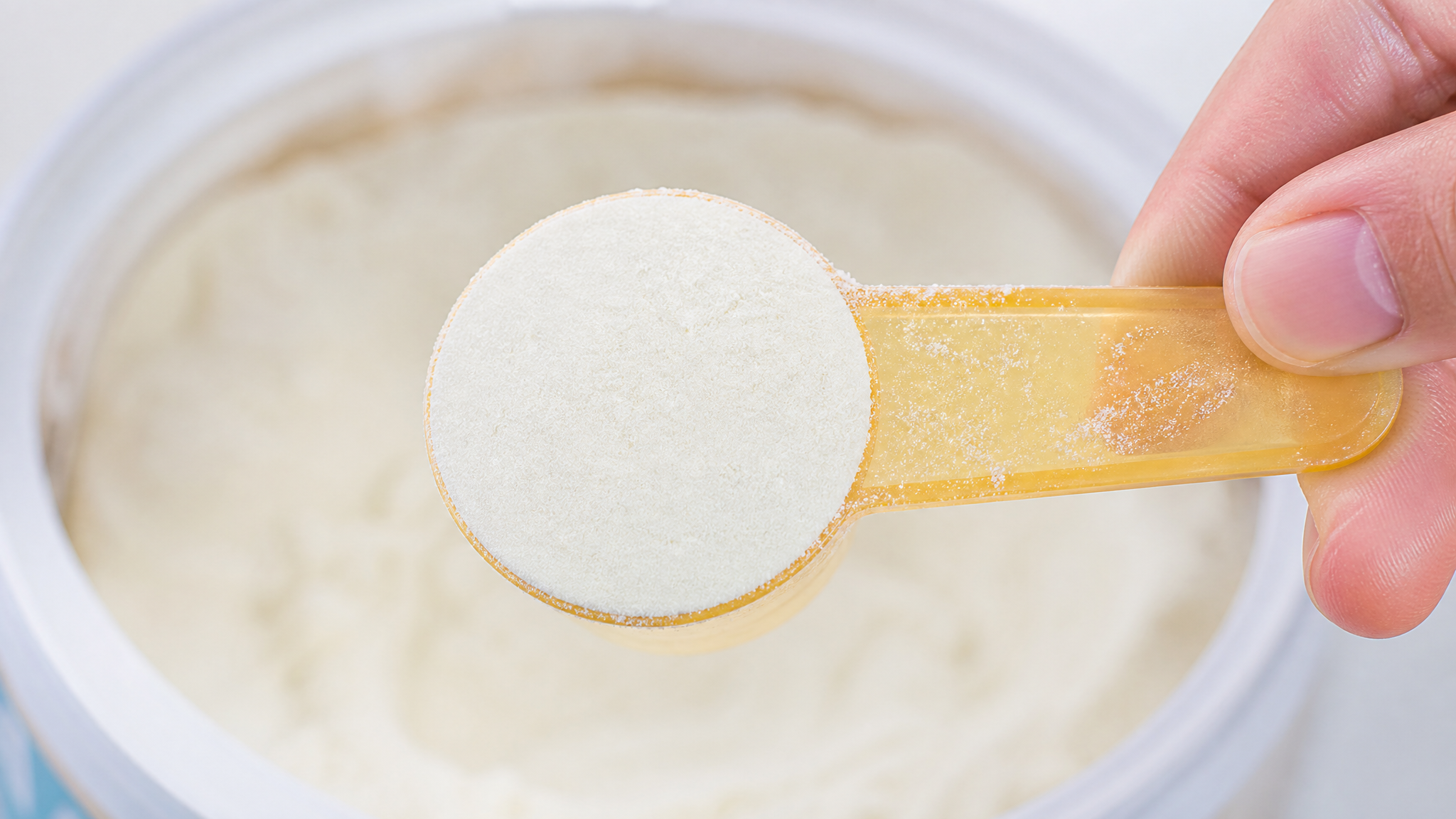 Extreme macro photography of a perfect flat scoop of baby formula powder held by a Chinese hand. Soft, clean studio lighting, bright and clinical atmosphere, highlighting the precise measurement. High resolution, 8k, photorealistic.