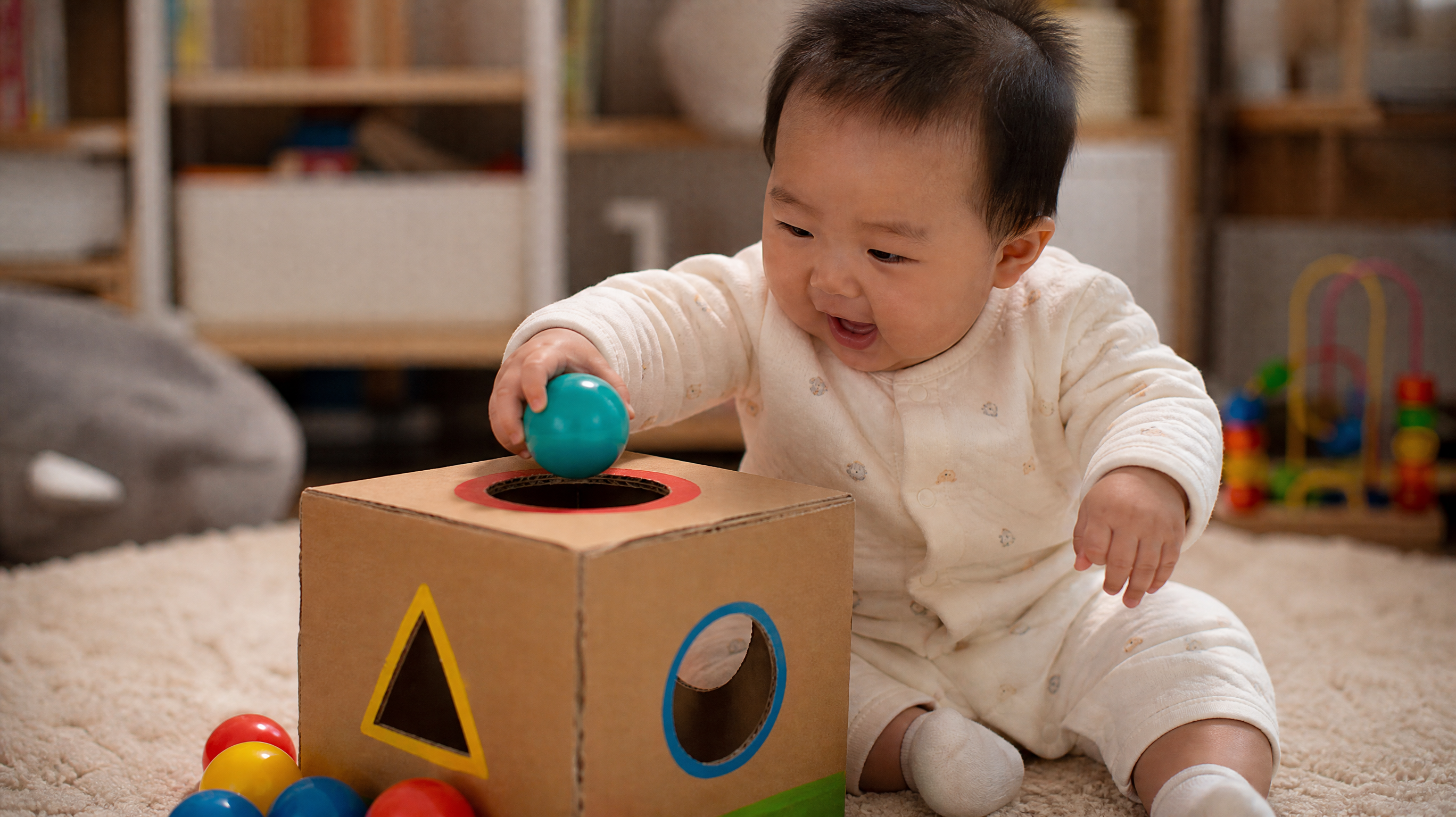 A cute 10-month-old Chinese baby focused on putting a colorful plastic ball into a hole on a homemade cardboard toy, sitting on a soft rug, warm indoor lighting, joyful expression, depth of field, highly detailed, realistic photography, 4k.