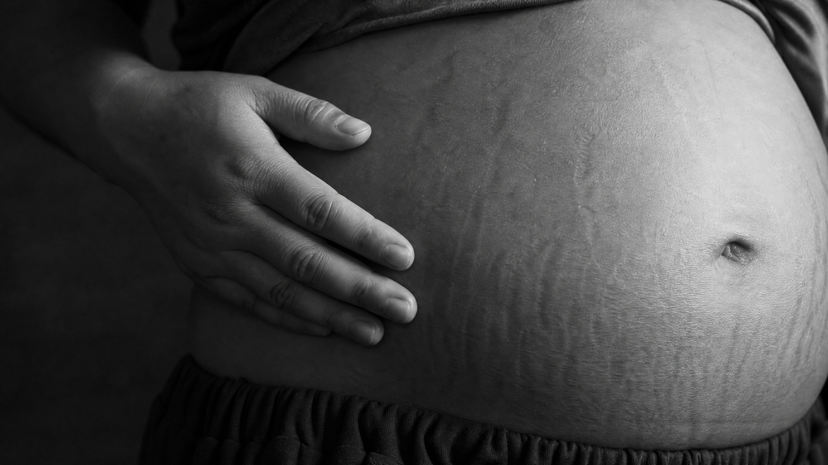 High quality black and white macro photography, close-up of a Chinese mother's postpartum belly, showing natural stretch marks and skin texture, a gentle hand pressing softly on the stomach, conveying strength and authenticity, film grain effect, cinematic lighting, profound and solemn atmosphere, 8k resolution, photorealistic. --ar 4:3