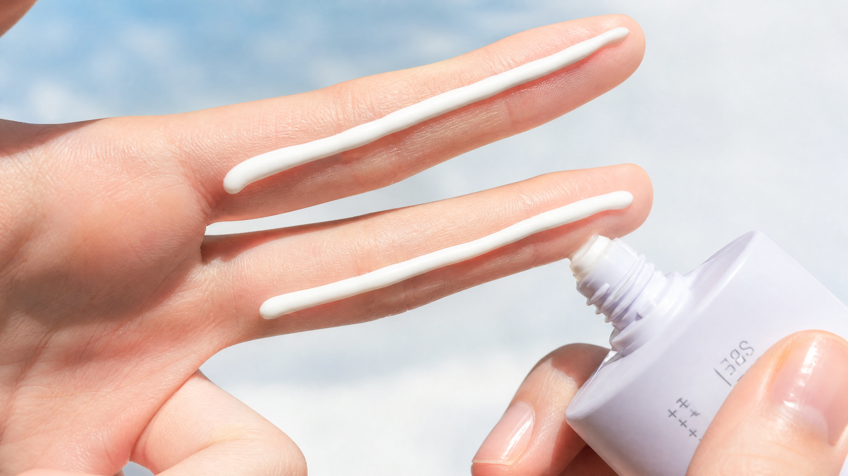 Close-up shot of a young Chinese woman's hand, squeezing white sunscreen lotion along the full length of her index and middle fingers (the