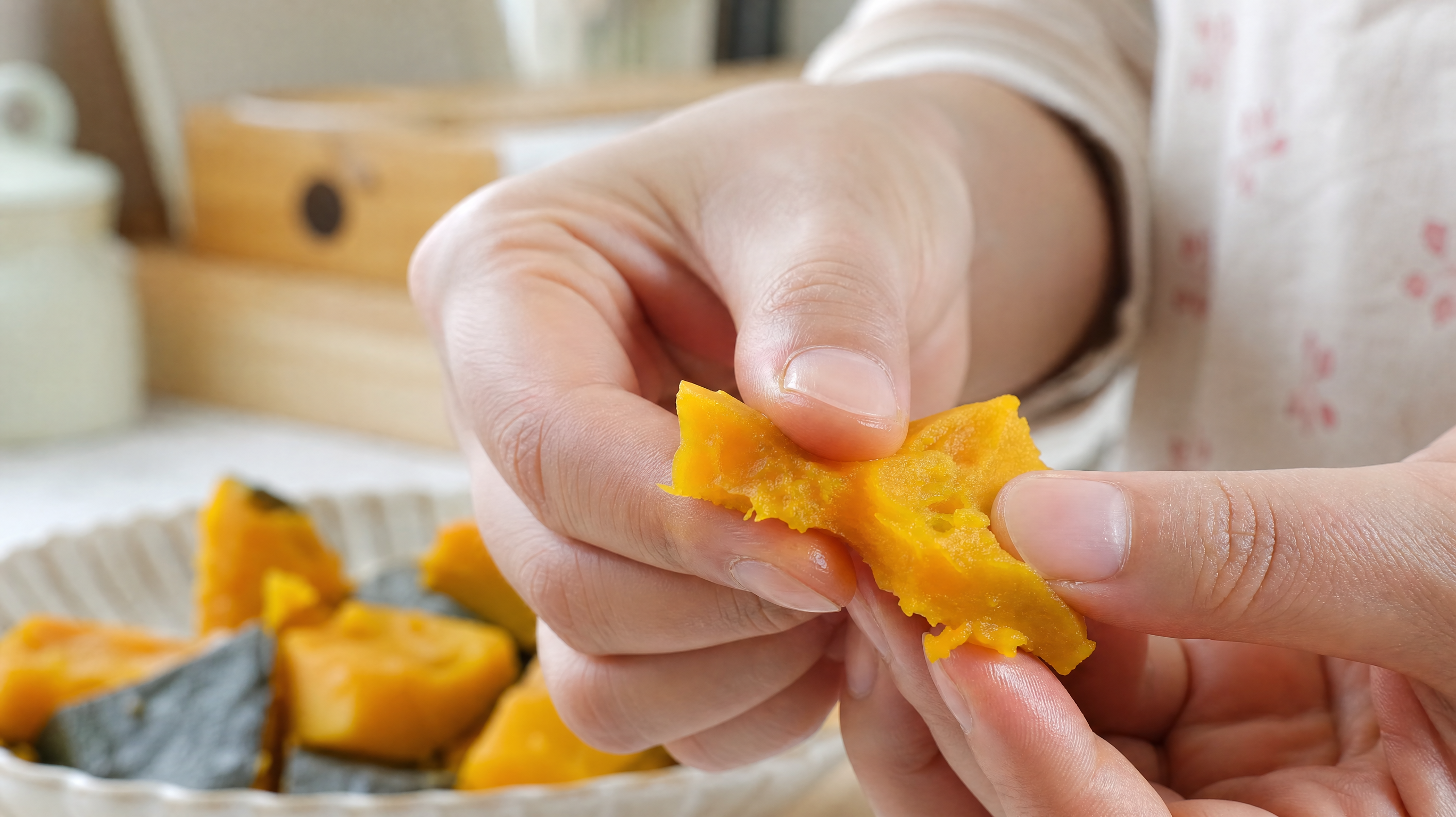 Close up shot of a Chinese mother's hands gently squeezing a piece of steamed pumpkin between her thumb and index finger, showing the softness of the baby food, bright and clean kitchen background, macro photography, soft natural light, highly detailed, 4k.