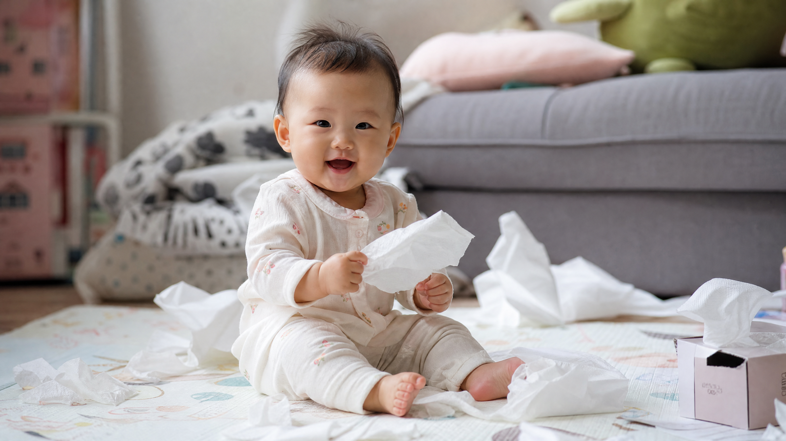 A cute 8-month-old Chinese baby sitting on a play mat, surrounded by torn pieces of tissue paper, holding a piece of paper playfully, soft natural lighting, cozy home environment, high quality, photorealistic, 8k, shot with 85mm lens.