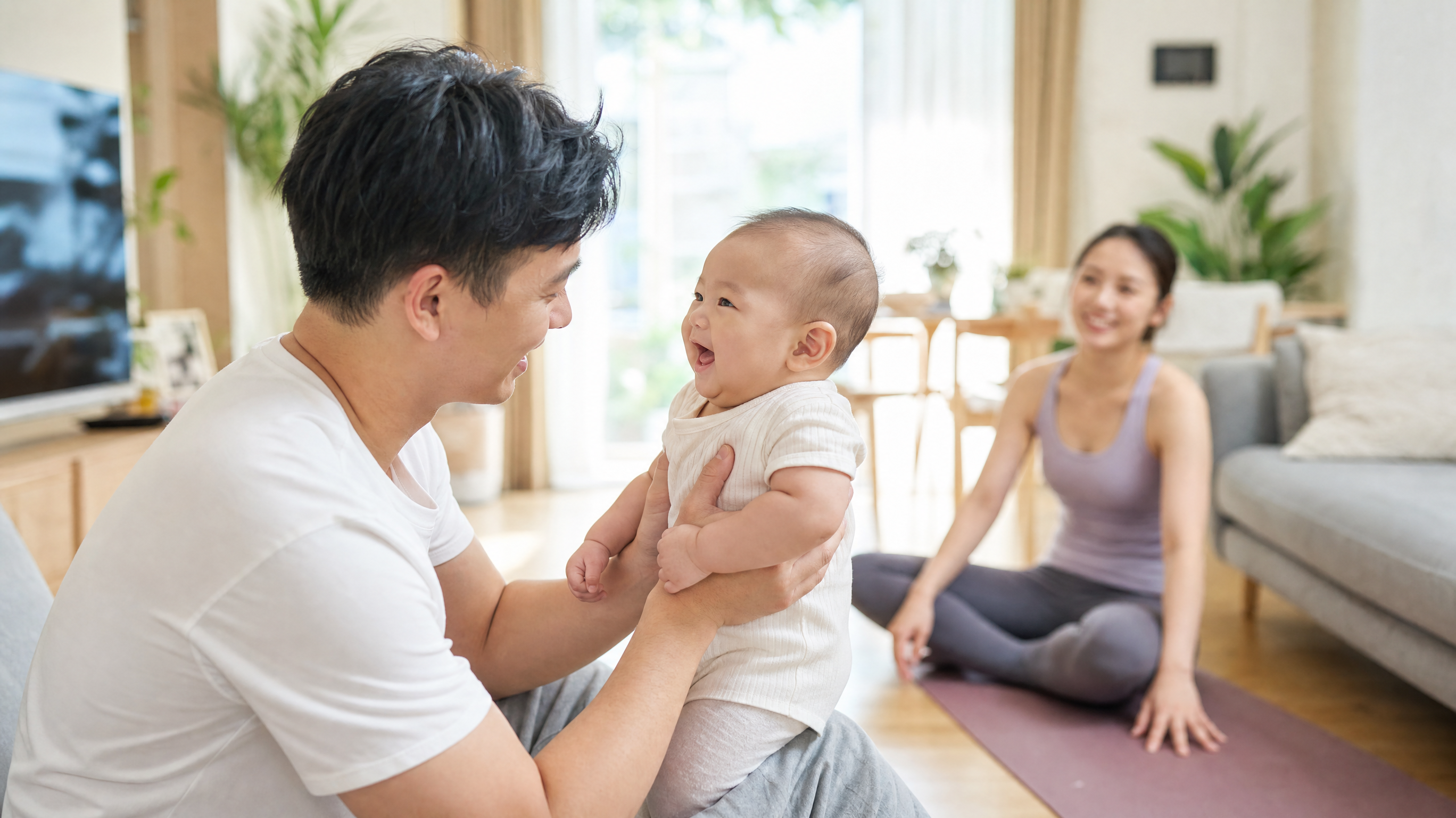 A heartwarming photorealistic image of a young Chinese father holding and gently playing with a cute baby in a bright living room, while the mother is seen in the blurred background relaxing on a yoga mat. Cozy home atmosphere, warm lighting, highly detailed, 8k.